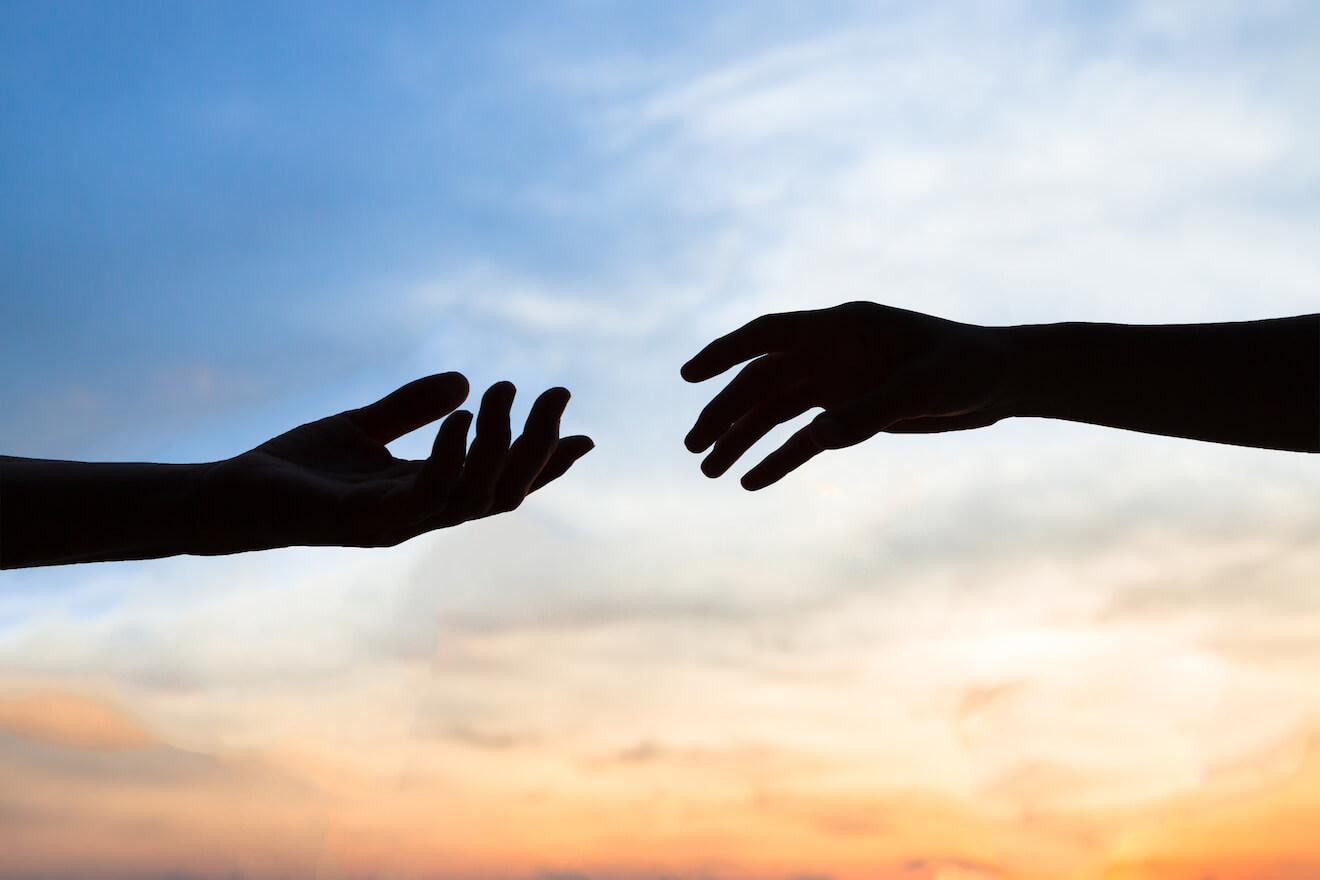 Hands reaching out to each other with a sunset background