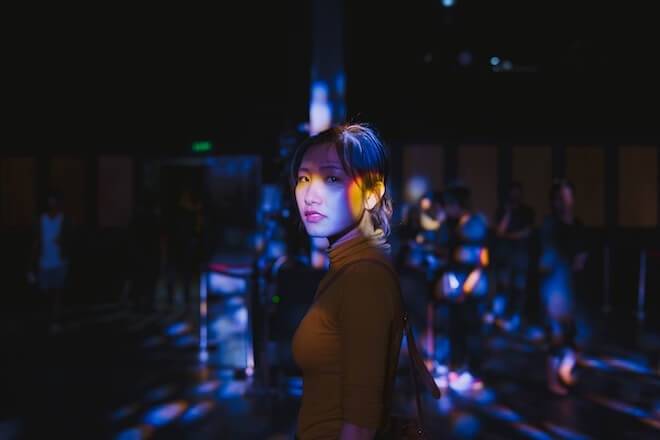 A woman looks pensive in the dark with colored light around her body