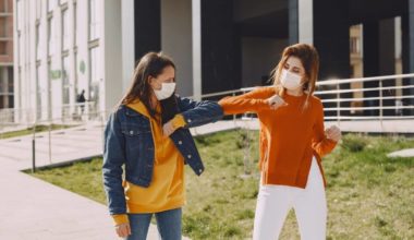 two women wearing masks and elbow bumping each other