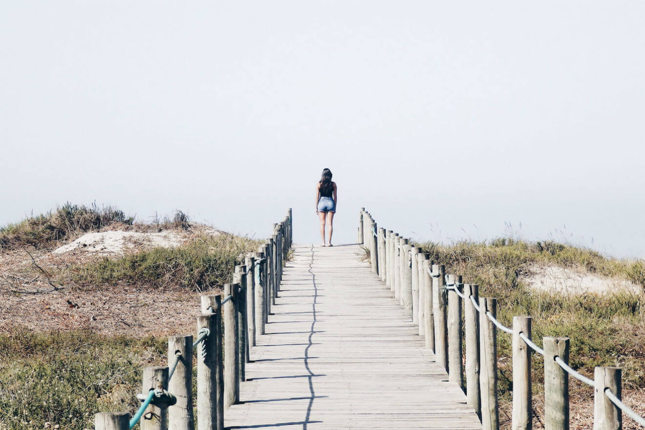 Woman walking long path leading up to beach
