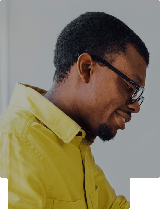 Side profile of a man in a yellow shirt and glasses slightly smiling and looking down