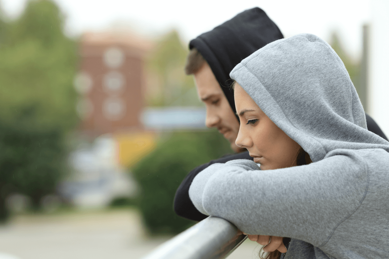 couple wearing hoodies leaning on bridge railing