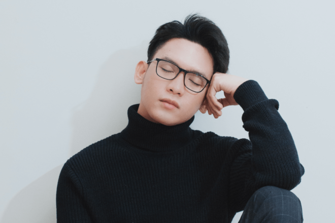 A stylish man leans his head against his hand with his eyes closed