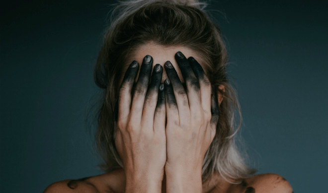 woman covering her face with her hands covered in black ink